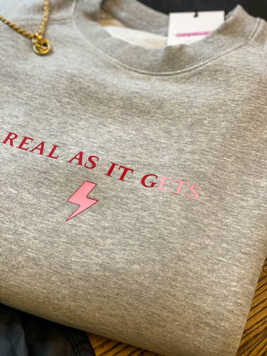 Grey-sweatshirt-close-up-slogan-Real-as-it-gets-with-pink-thunderbolt-detail