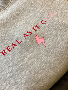 Grey-sweatshirt-close-up-slogan-Real-as-it-gets-with-pink-thunderbolt-detail