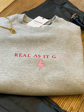 Load image into Gallery viewer, Grey-sweatshirt-close-up-slogan-Real-as-it-gets-with-pink-thunderbolt-detail
